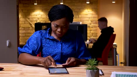 Closeup-shoot-of-adult-african-american-businesswoman-texting-on-the-tablet-in-the-office-indoors-on-the-workplace