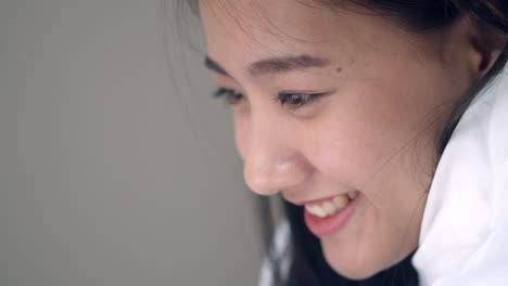 Close-up-portrait-Asian-woman-smiling-and-using-a-tablet-on-the-bedroom-browsing-online-social-media-sharing-lifestyle.