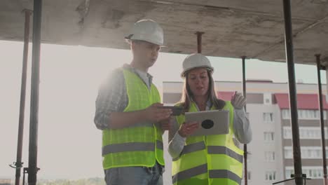 Supervisor-de-un-edificio-en-construcción-discutiendo-con-la-diseñadora-de-ingeniería-el-progreso-de-la-construcción-y-examina-un-plan-de-construcción