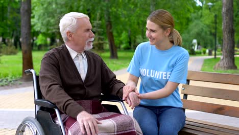 Freundliche-junge-Frau-freiwillige-T-shirt-hält-behinderte-männliche-Hand,-Patientenunterstützung