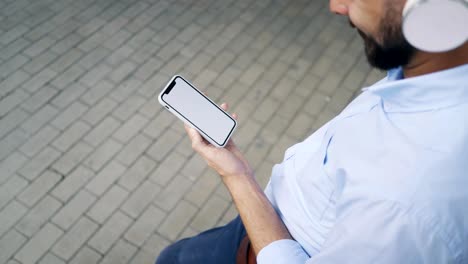 Vista-superior-del-hombre-en-los-auriculares-mirando-el-teléfono-inteligente-mientras-está-en-la-ciudad