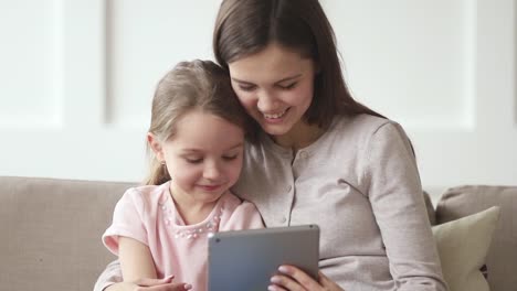 Happy-mom-and-kid-daughter-watching-funny-cartoons-on-tablet