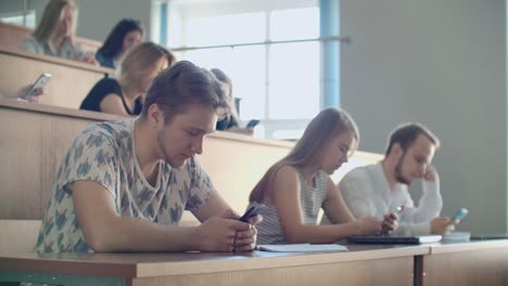 Grupo-multiétnico-de-estudiantes-que-utilizan-teléfonos-inteligentes-durante-la-conferencia.-Jóvenes-que-usan-las-redes-sociales-mientras-estudian-en-la-Universidad.