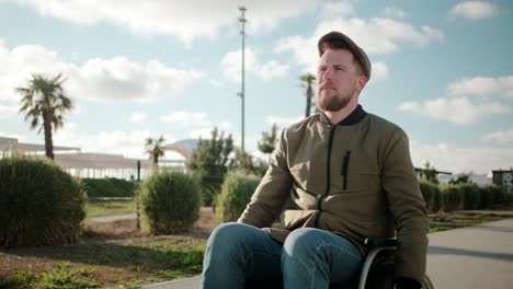 Confident-bearded-man-is-riding-on-wheelchair-outdoors-alone-in-sunny-day