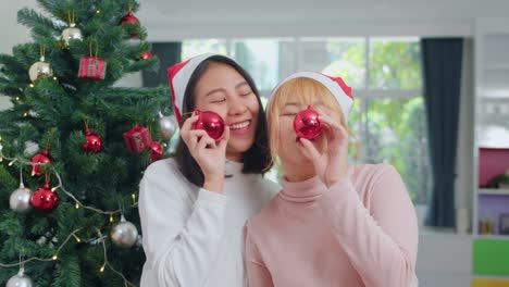 Asian-Lesbian-couple-celebrate-Christmas-festival.-LGBTQ-female-teen-wear-Christmas-hat-relax-happy-play-Christmas-ball-enjoy-xmas-winter-holidays-together-in-living-room-at-home.-Slow-motion-shot.