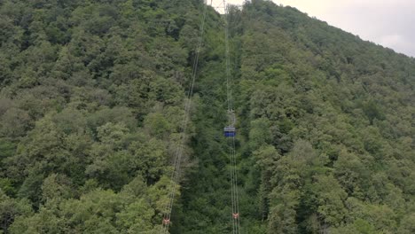 Cable-car-cabin-working-in-green-mountain-summer-resort-aerial-view.-Cable-car-moving-to-peak-green-mountain-among-forest-trees.-Rope-way-in-mountain-resort