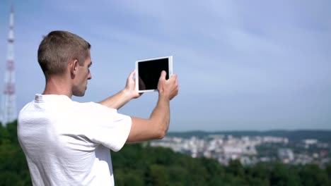 attraktiver-junger-Mann-fängt-das-umliegende-Panorama-auf-einem-Tablet-ein