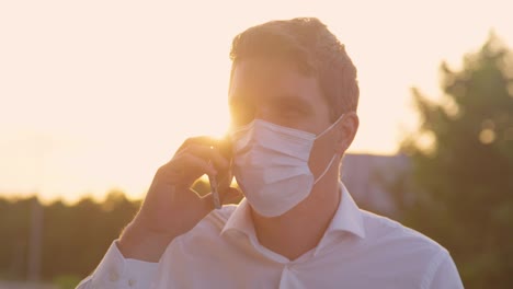 CLOSE-UP:-Young-man-talks-on-the-phone-while-wearing-a-disposable-surgical-mask.