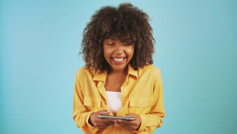 Afro-american-mujer-jugando-videojuego-en-el-teléfono-inteligente-y-sonriendo-mientras-posan-contra-el-fondo-de-estudio-azul