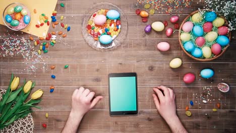 Man-using-digital-tablet-on-table-decorated-with-easter-eggs.-Top-view