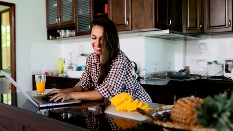 Chica-uso-portátil-en-cocina-chateando-en-línea-joven-estudio-casa-moderna-Interior