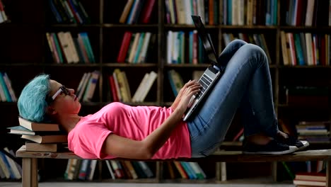 Nettes-Mädchen-mit-Laptop-auf-Bank-in-Bibliothek-liegend