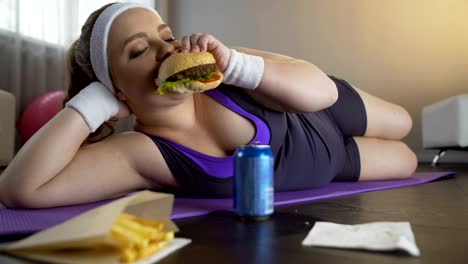 Chica-obesa-seguro-de-sí-mismo-feliz-comiendo-grasa-hamburguesa-en-lugar-de-entrenamiento-de-deportes