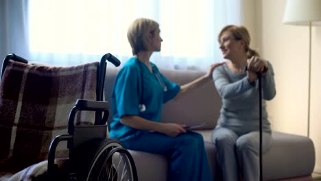 Nurse-and-aged-woman-sitting-on-sofa-at-hospital,-discussing-news,-support