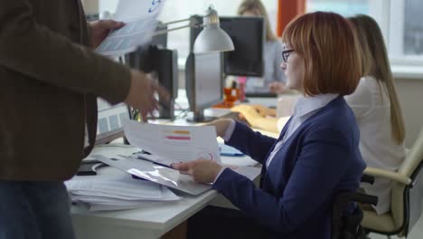 Mujer-en-silla-de-ruedas-sobre-documentos-de-negocios-con-un-colega-masculino