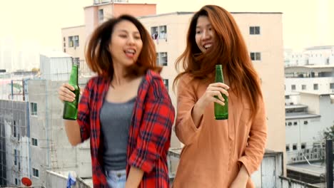 Young-asian-woman-lesbian-couple-dancing-and-clinking-bottles-of-beer-party-on-rooftop.