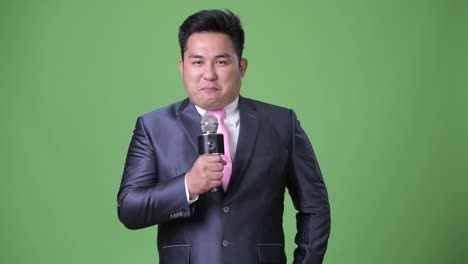 Young-handsome-overweight-Asian-businessman-against-green-background