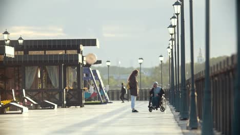 Hombre-discapacitado-en-silla-de-ruedas-hablar-por-teléfono,-caminar-juntos-a-su-novia-en-el-muelle