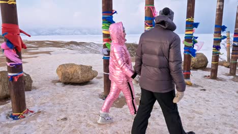 Joven-pareja-caminando-disfrutando-al-aire-libre-en-las-montañas-superiores-de-invierno.-Polos-de-Ritual-budista-con-cintas-de-colores-en-el-invierno-en-el-sitio-sagrado-del-lago-Baikal.