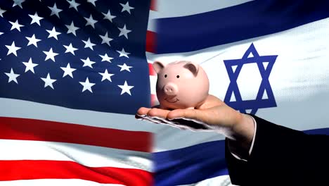 US-investment-in-Israel,-hand-putting-money-in-piggybank-on-flag-background