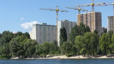 Ein-See-vor-dem-Hintergrund-der-Häuser-im-Bau.-Wolkenkratzer-sind-in-der-Nähe-des-Sees-gebaut.-Bau-von-Wohngebäuden-in-der-Nähe-des-Sees.