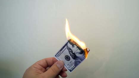 Mano-que-sostiene-un-billete-de-cien-dólares-ardiente