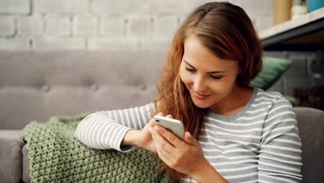 Happy-young-woman-is-holding-smartphone-touching-screen-and-smiling-checking-social-media-account-or-reading-messages.-Modern-technology-and-millennials-concept.