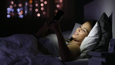 Glückliches-Mädchen-chatten-in-einem-Telefon-im-Bett-in-der-Nacht