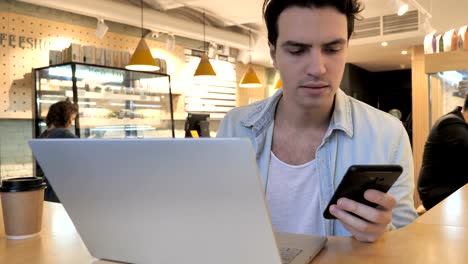 Junger-Mann-arbeiten-am-Laptop-und-Smartphone-in-Café