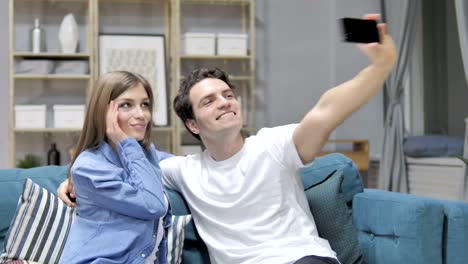 Joven-pareja-teniendo-Selfie-con-Smartphone-mientras-está-sentado-en-el-sofá