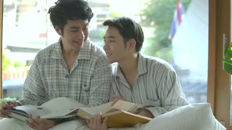 Young-asian-gay-couple-sitting-on-the-windowsill-and-reading-book-at-home-in-the-morning.