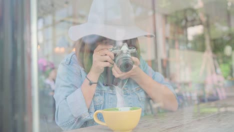 Food-blogger-Asian-woman-using-camera-for-photo-dessert,-bread-and-drink-while-sitting-on-table-in-cafe.-Lifestyle-beautiful-women-relax-at-coffee-shop-concepts.