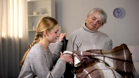 Granddaughter-gently-covering-with-plaid-granny-sleeping-in-wheelchair,-family