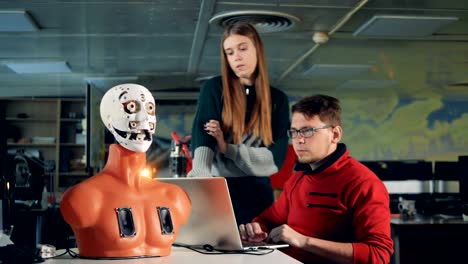 Man-and-woman-work-with-bionic-robot-in-a-room,-close-up.