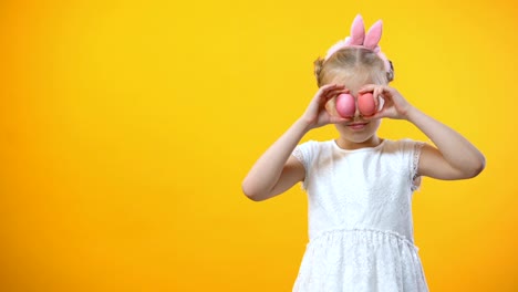 Happy-Easter-greetings,-smiling-little-girl-holding-colored-eggs-in-front-eyes