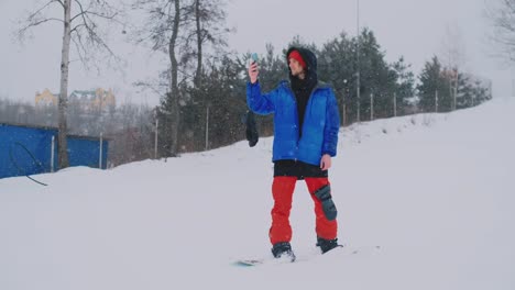 Slow-motion-shot-of-a-snowboarder-using-a-smartphone-while-driving-on-a-ski-slope