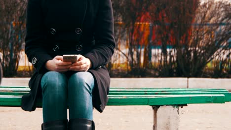 Junges-Mädchen-mit-einem-Handy-auf-einer-Bank-im-Stadtpark