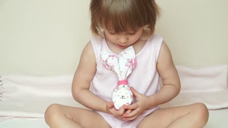 Portrait-of-cute-smiling-baby-girl-sits-and-shows-chicken-eggs-in-hands,-decorated-for-Easter-bunny,-with-painted-muzzle.