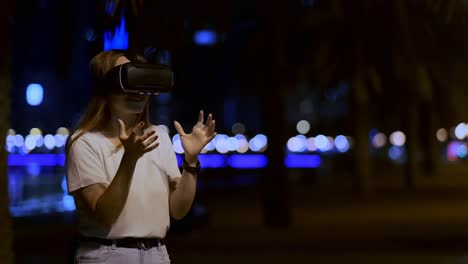 Junge-Frau-in-Virtual-Reality-Brille-in-der-Nachtstadt-bewegt-ihre-Hände