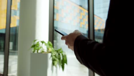 Tracking-left-shot-of-unrecognizable-businessman-in-suit-texting-on-smartphone-while-walking-along-entrance-hall-in-office-building