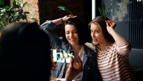 Weibliche-Freunde-fotografieren-im-Café-posiert-mit-Grimassen-mit-Smartphone