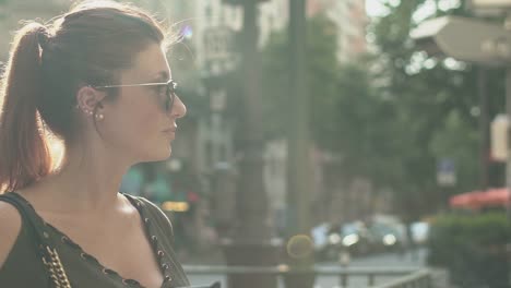 Attractive-redhead-girl-woman-with-freckles-and-red-hair-turning-head-at-left-then-right-and-writing-text-message-on-her-smartphone-at-subway-exit-in-street,-during-sunny-summer-in-Paris.-Slow-motion.