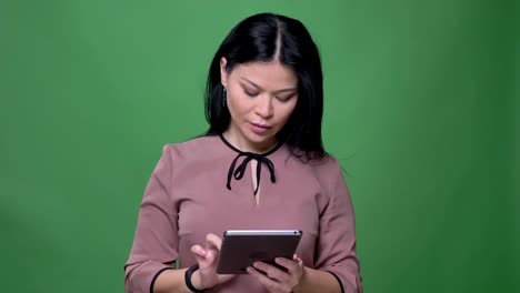 Closeup-shoot-of-young-attractive-asian-female-with-black-hair-using-the-tablet-with-background-isolated-on-green