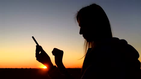 Frau-Silhouette-mit-Smartphone-in-der-Stadt-bei-Sonnenuntergang