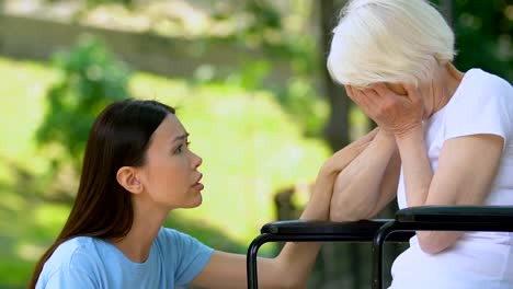 Female-volunteer-supporting-crying-elderly-female-in-wheelchair-in-hospital-park