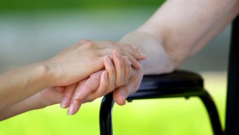 Daughter-supporting-her-disabled-mother-tenderly-stroking-her-hand,-close-up