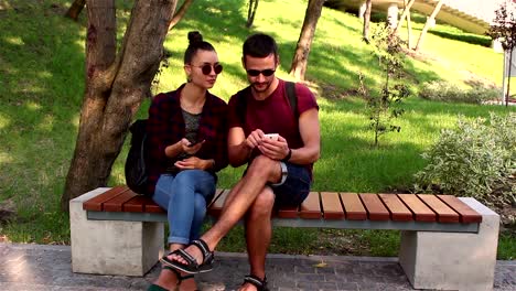 Pareja-en-el-amor-mostrar-fotos-en-sus-teléfonos-inteligentes,-sentado-en-un-banco-del-parque.