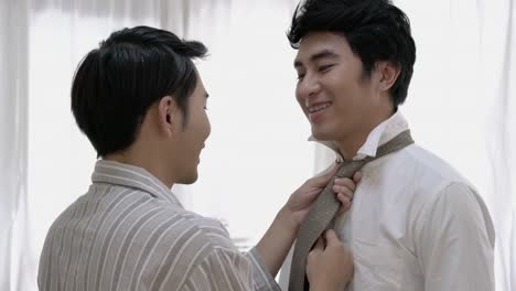 Asian-couple-gay-helping-tie-a-necktie-and-dress-to-work-in-morning-at-home.-Gay-boy-happy-emotion-and-hug-love-anniversary-together.-Concept-of-lifestyle,-family,-gay-and-bisexual.