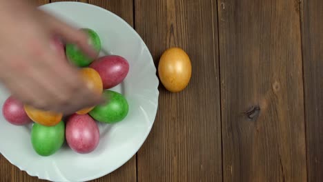 A-person-lays-colored-multi-colored-chicken-eggs-on-a-plate,-wooden-background,-Easter-holiday,-copy-space,-homemade