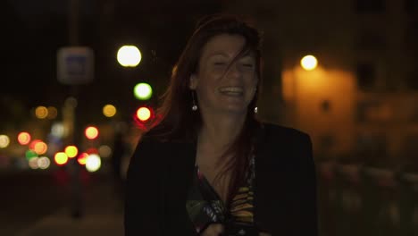 Caucasian-modern-woman-wearing-flower-dress,-black-jacket-and-red-hair-walking-through-the-street-and-writing-a-text-message-and-laughing-on-her-smartphone-by-night.-Paris-4K-UHD.-Slow-Motion.